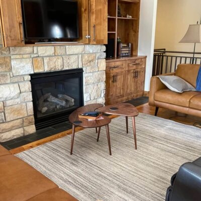 A modular nesting coffee table set featuring a walnut hardwood medium kidney bean table and a guitar pick table styled in a modern living room by a stone fireplace, linking to the custom living room coffee table gallery.