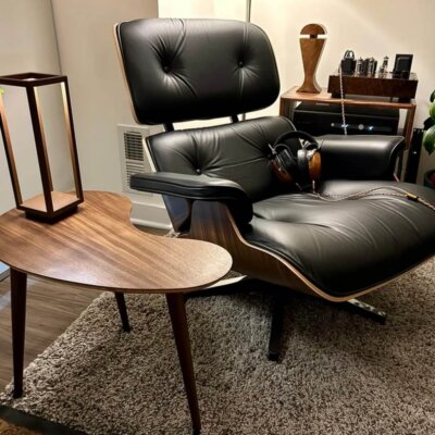 Custom mid-century modern walnut kidney bean side table styled next to a black leather Eames lounge chair in an audiophile listening room, linking to the custom side table furniture collection.